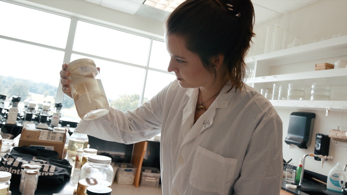 一个在实验室工作的女学生，她拿着罐子里的样品。