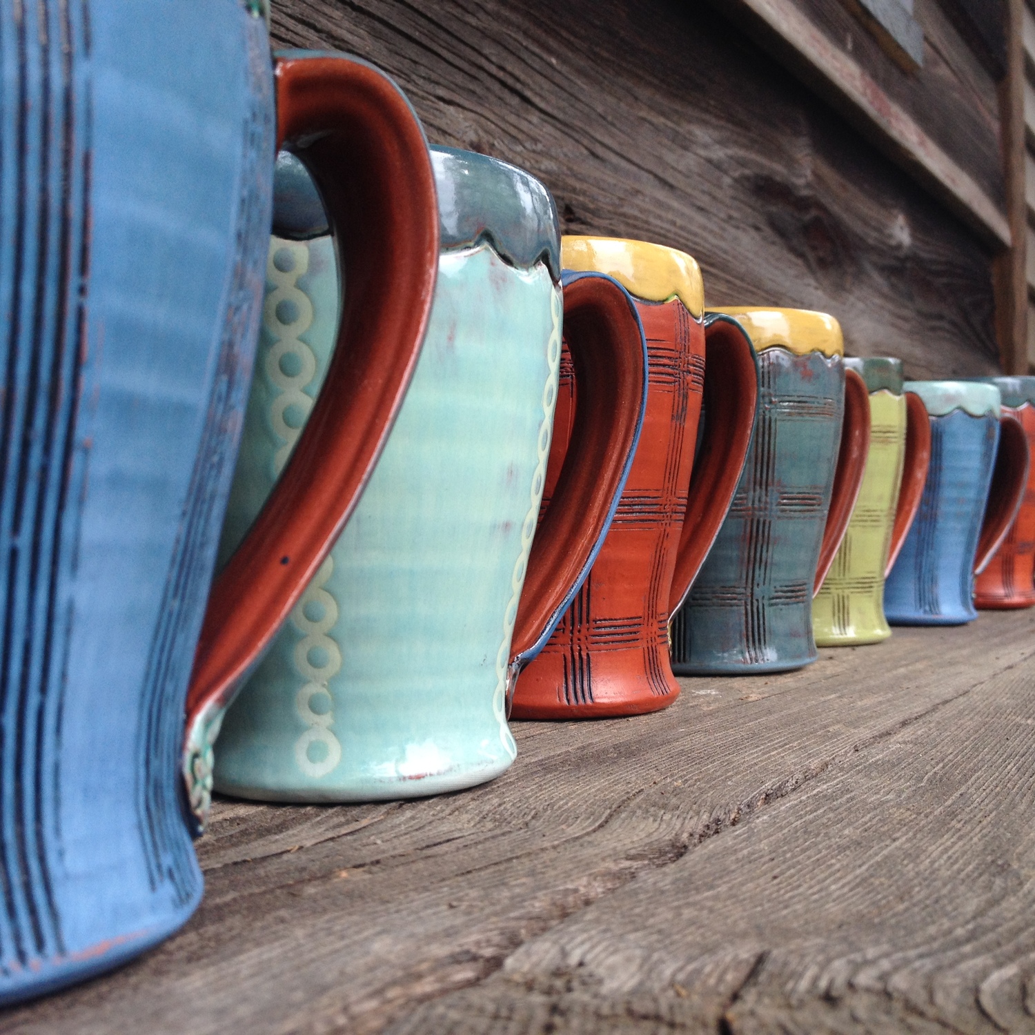 由艺术家艾米·桑德斯创作的一排充满活力的彩色陶瓷咖啡杯。
