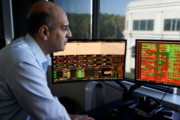 一个特写的照片一个年长的男研究生操作数据在桌子和几个电脑显示器。