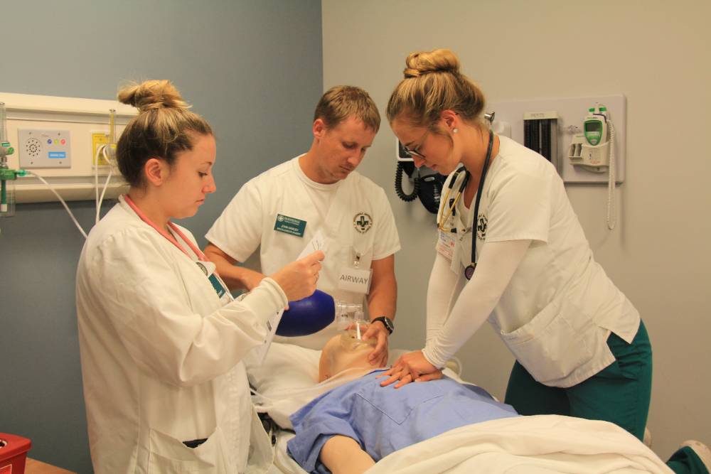 三个学生在健康模拟中心练习心肺复苏术。