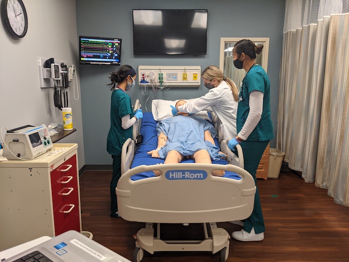 在模拟中心，三个护理学生在模型病人身上练习。