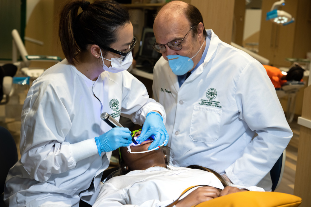 一个学生给病人做牙科检查，教授在一旁看着。